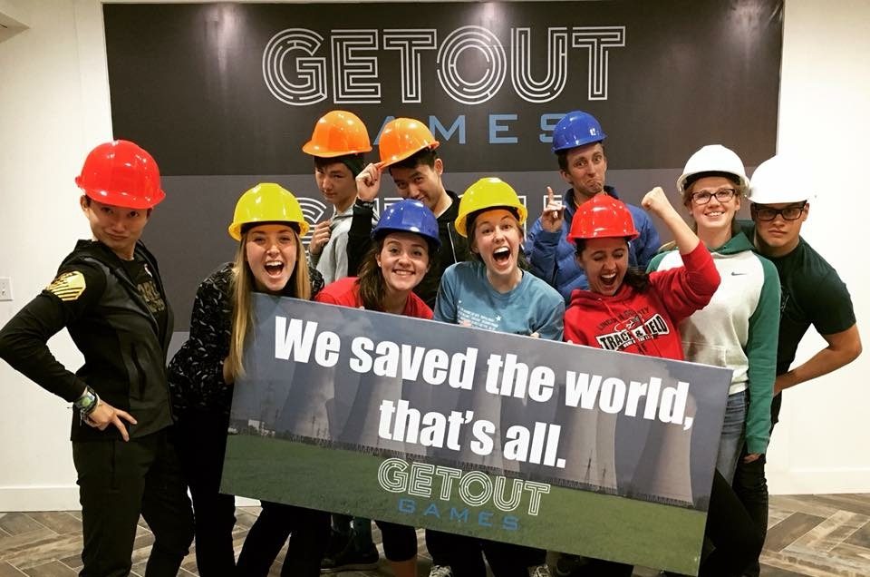 happy group of friends celebrate finishing an escape room and and hold a sign that says "We saved the world, that's all."